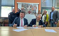 Schulleiter Jochen Herkert und DRK-Präsident Gerhard Lauth unterzeichneten an einem Tisch sitzend eine Bildungspartnerschaft zwischen NKG und DRK-Kreisverband Mosbach. Bild: DRK