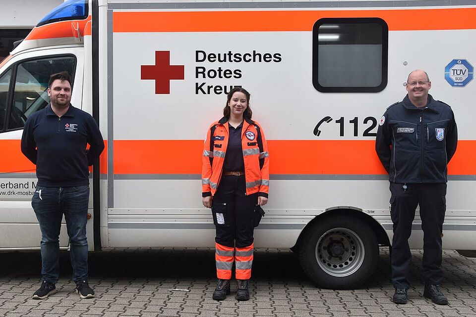 Yasmin El-Bougi (m.) mit ihren Ausbildern Robin Bracht (l.) und Henning Waschitschek (r.) vor einem Einsatzwagen an der Mosbacher DRK-Rettungswache in der Sulzbacher Straße. 