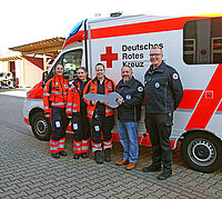 Notfallsanitäterinnen, der Kreisgeschäftsführer und der Leitstellenleiter mit einem symbolischen Schlüssel vor einem Rettungswagen