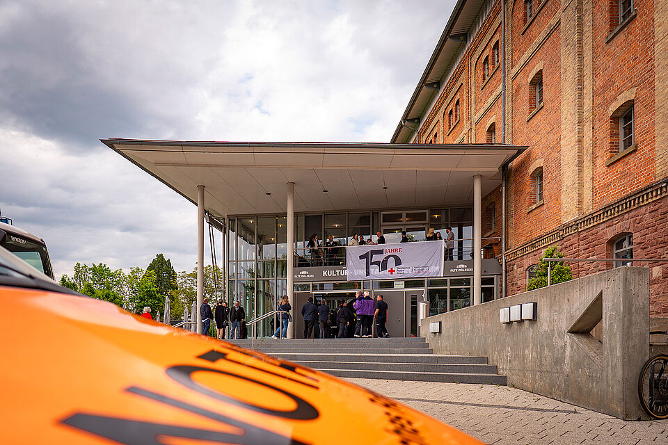 Notarztfahrzeug vor dem Tagungszentrum Alte Mälzerei in Mosbach. Am Eingang hängt die DRK-Fahne mit dem Jubiläums-Logo